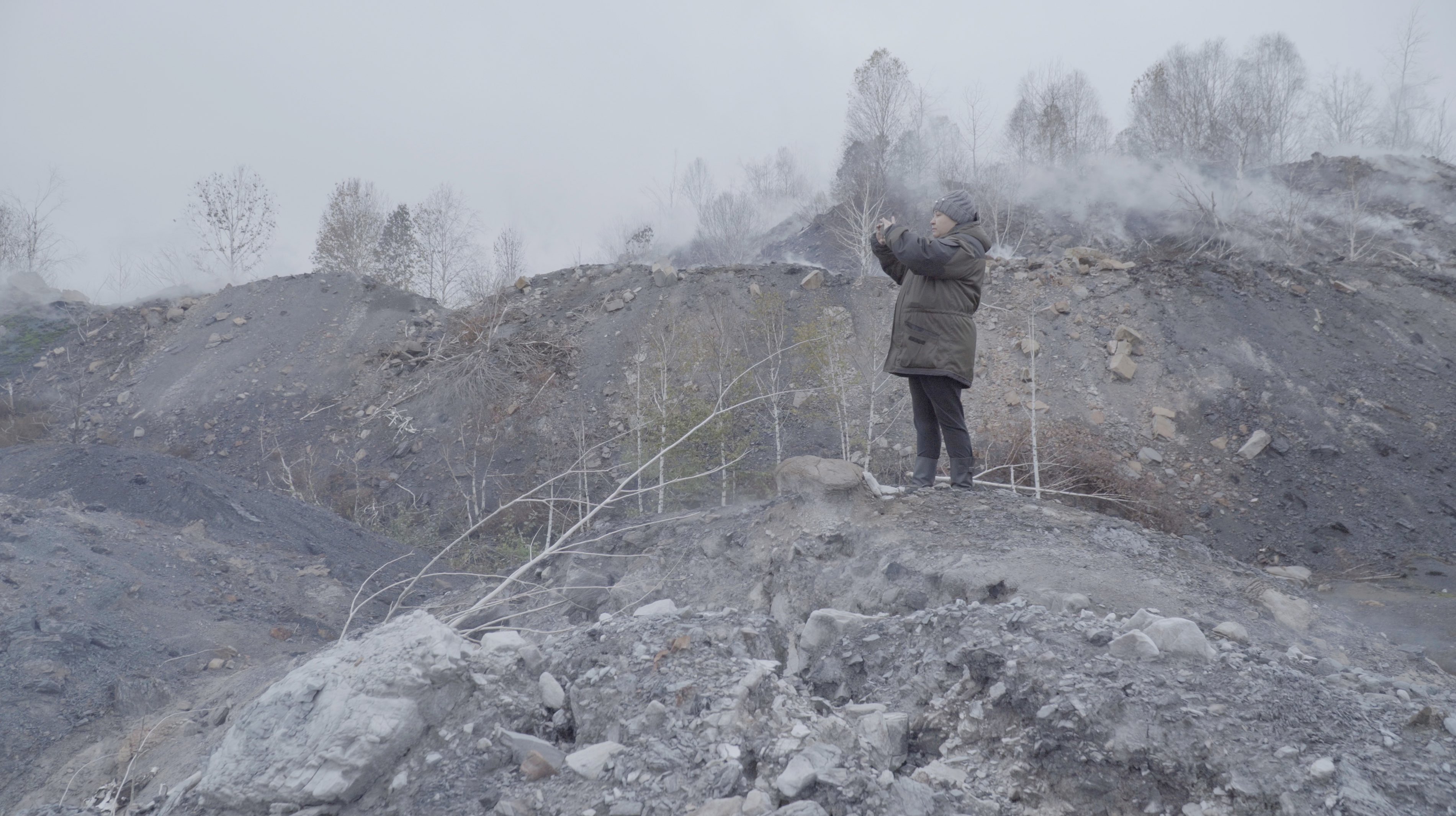 Een close-up van Natalia Zubkova met een reflecterende, ronde zonnebril met een metalen montuur. De reflectie in de glazen toont spoorrails die zich in de verte uitstrekken, omgeven door groene velden onder een heldere hemel.