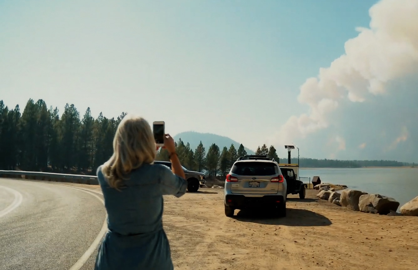 A woman captures the smoke of a forest fire in the distance with her mobile phone