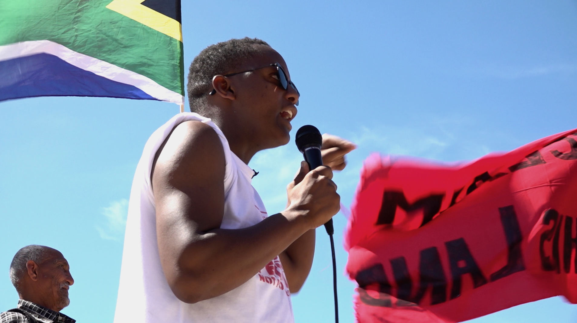 Activist Nkosikhona Swartbooi spreekt de menigte toe bij de Occupy Rondebosch Golfbaan actie
