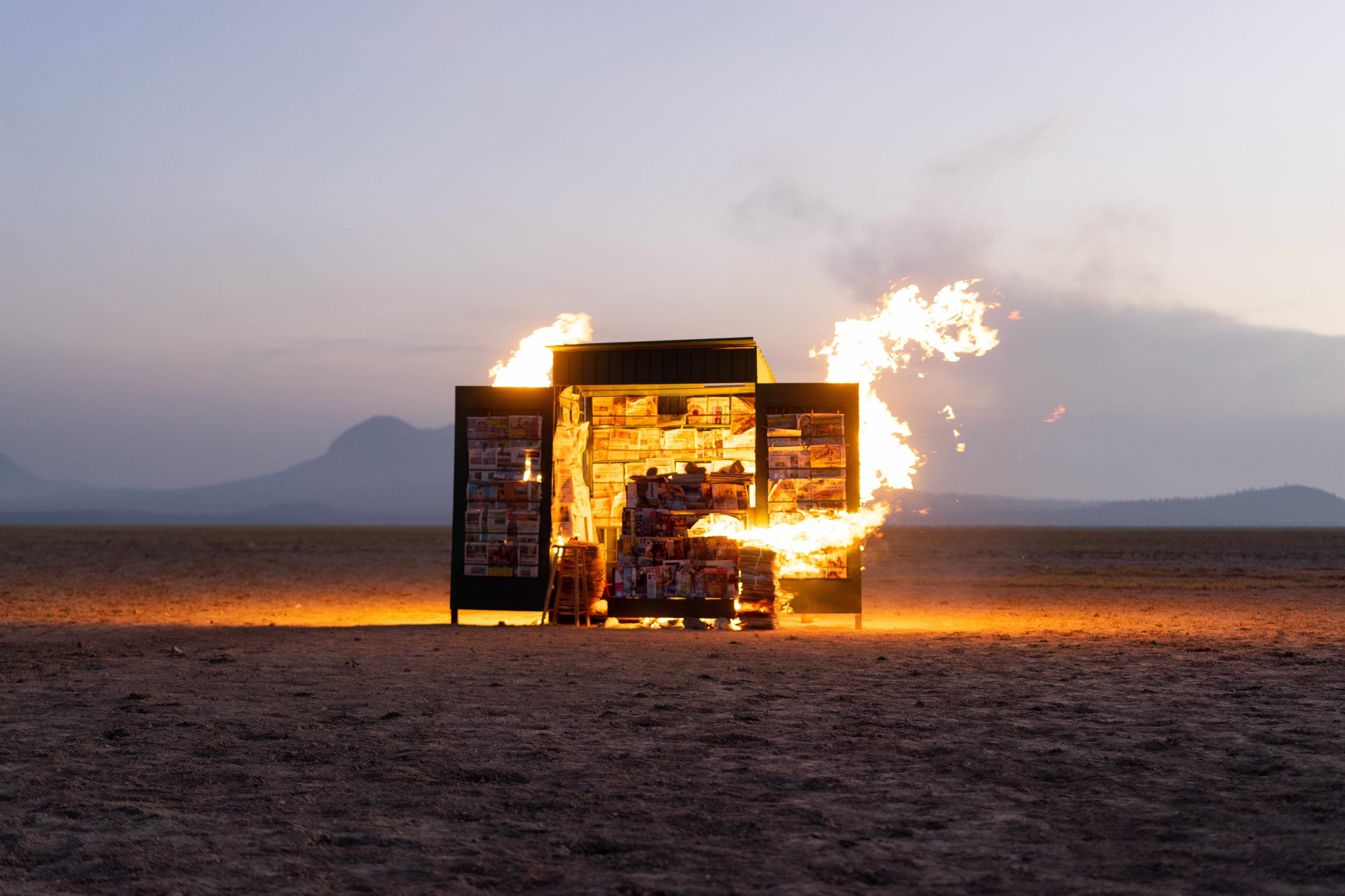 Een krantenkiosk staat in brand midden in een open veld